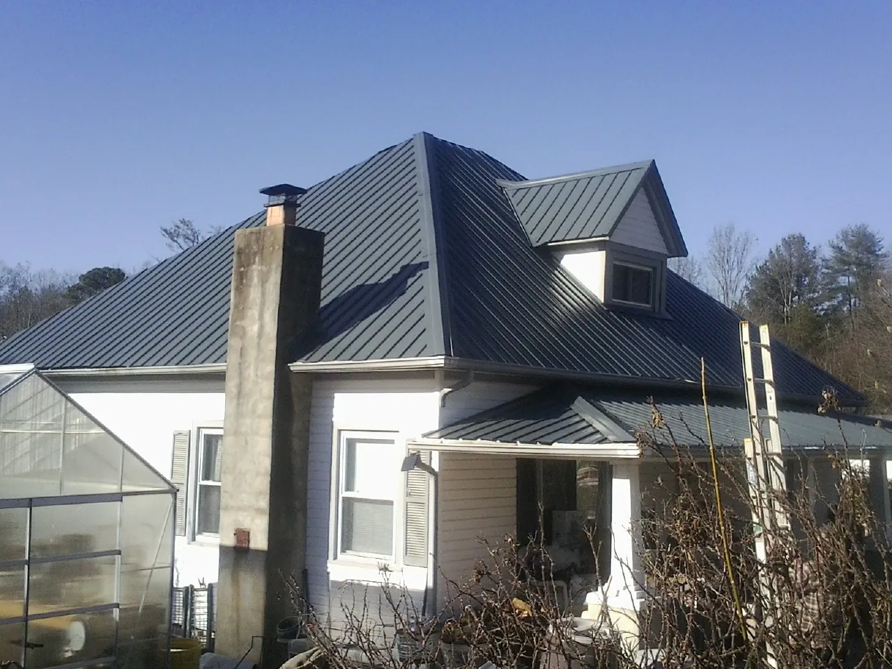 Dark blue standing seam metal roof on a white farmhouse with dormer — Slate & Tile Roof Repair by Roofing Brothers in Broussard