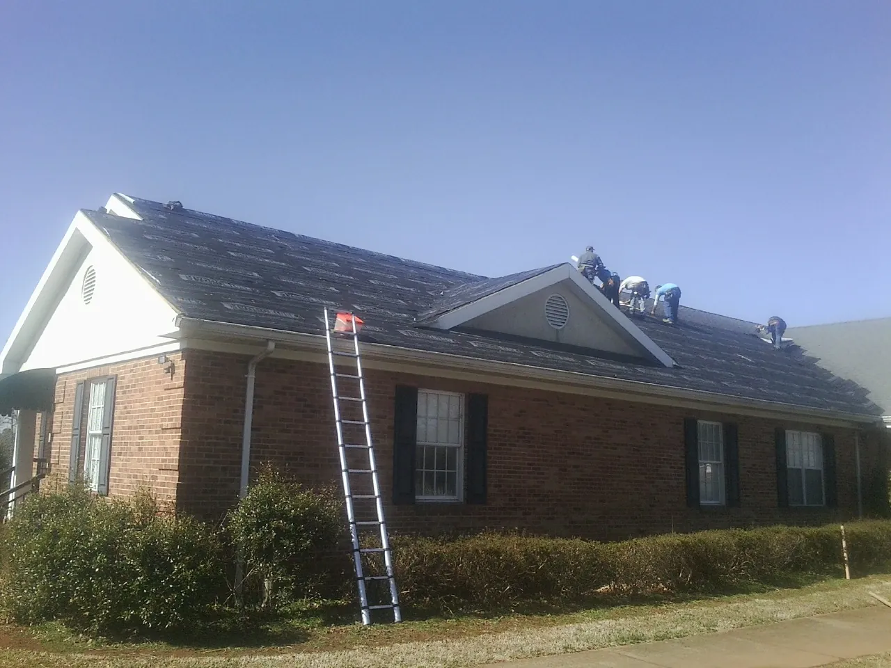 Crew tearing shingles off a brick ranch roof with a ladder set — Emergency Roof Repair work by our crew in Broussard
