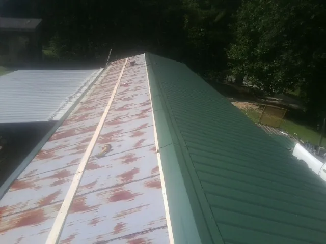 Old rusted panels beside newly installed green metal roofing — Wind Damage Roof Repair by Roofing Brothers in Broussard