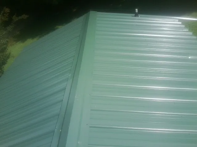 New green metal panels meeting at the ridge of a roof — Flat Roof Repair work by our crew in Broussard