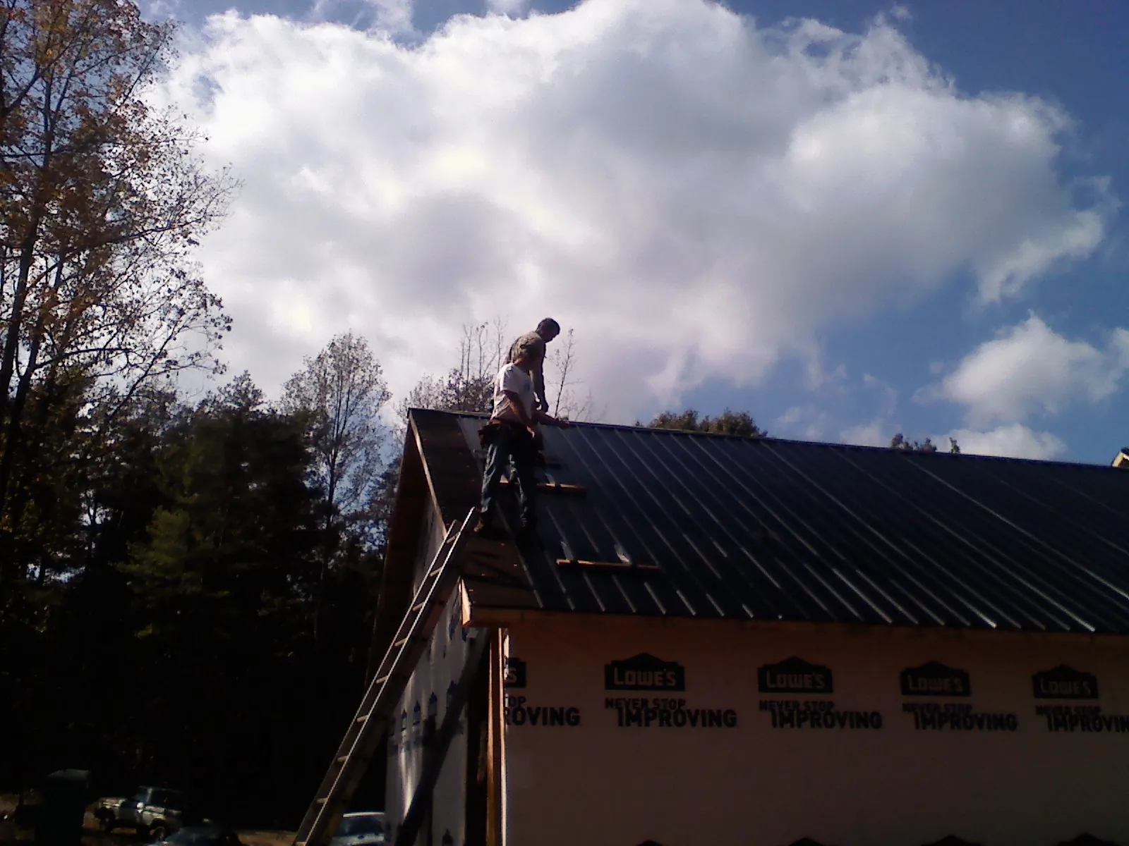 Roofer fastening dark metal panels high against a cloudy sky, from a Roof Inspection job in Broussard