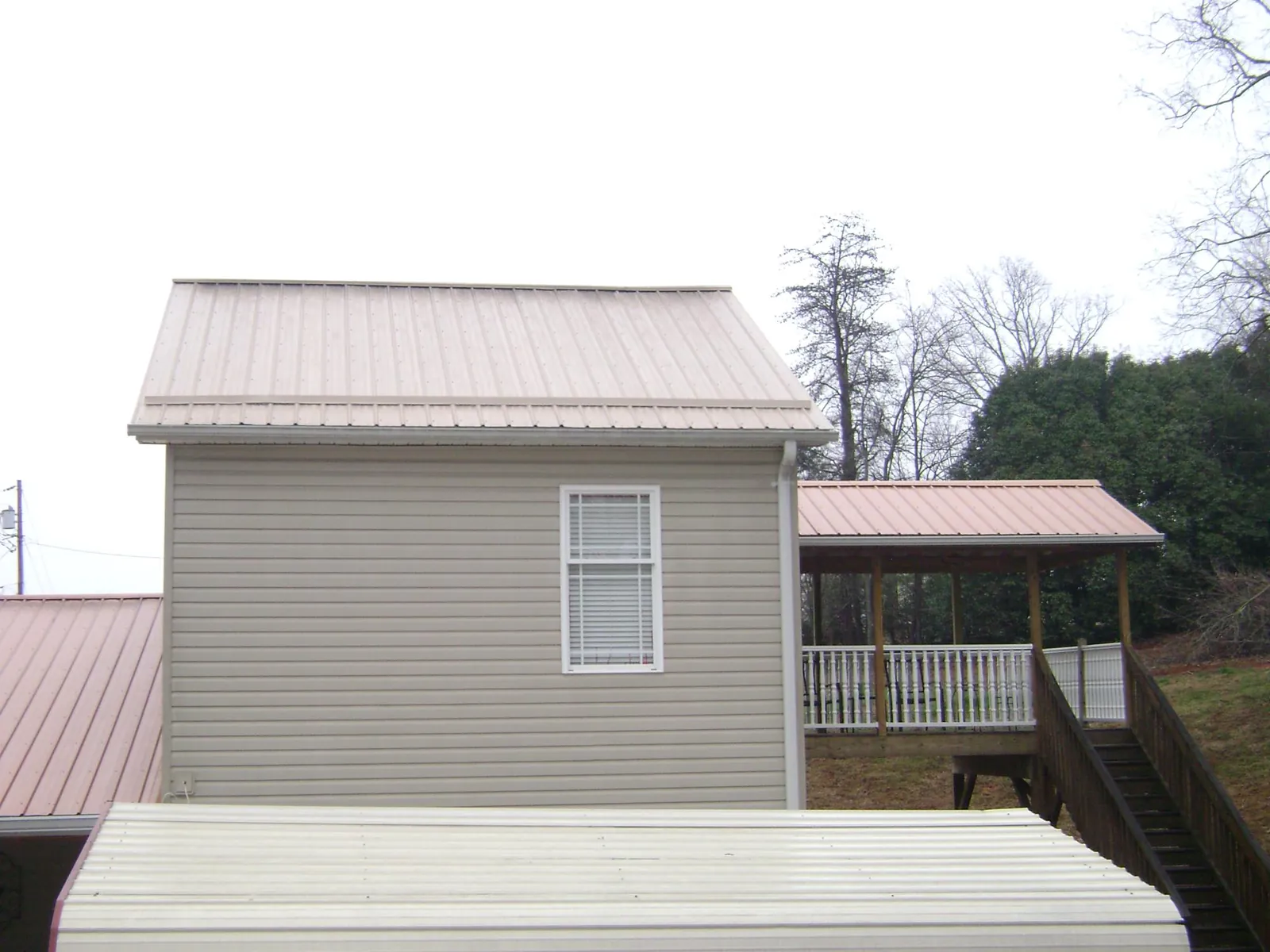 Tan metal roofs on a two story addition and attached porch, from a Roof Replacement job in Broussard